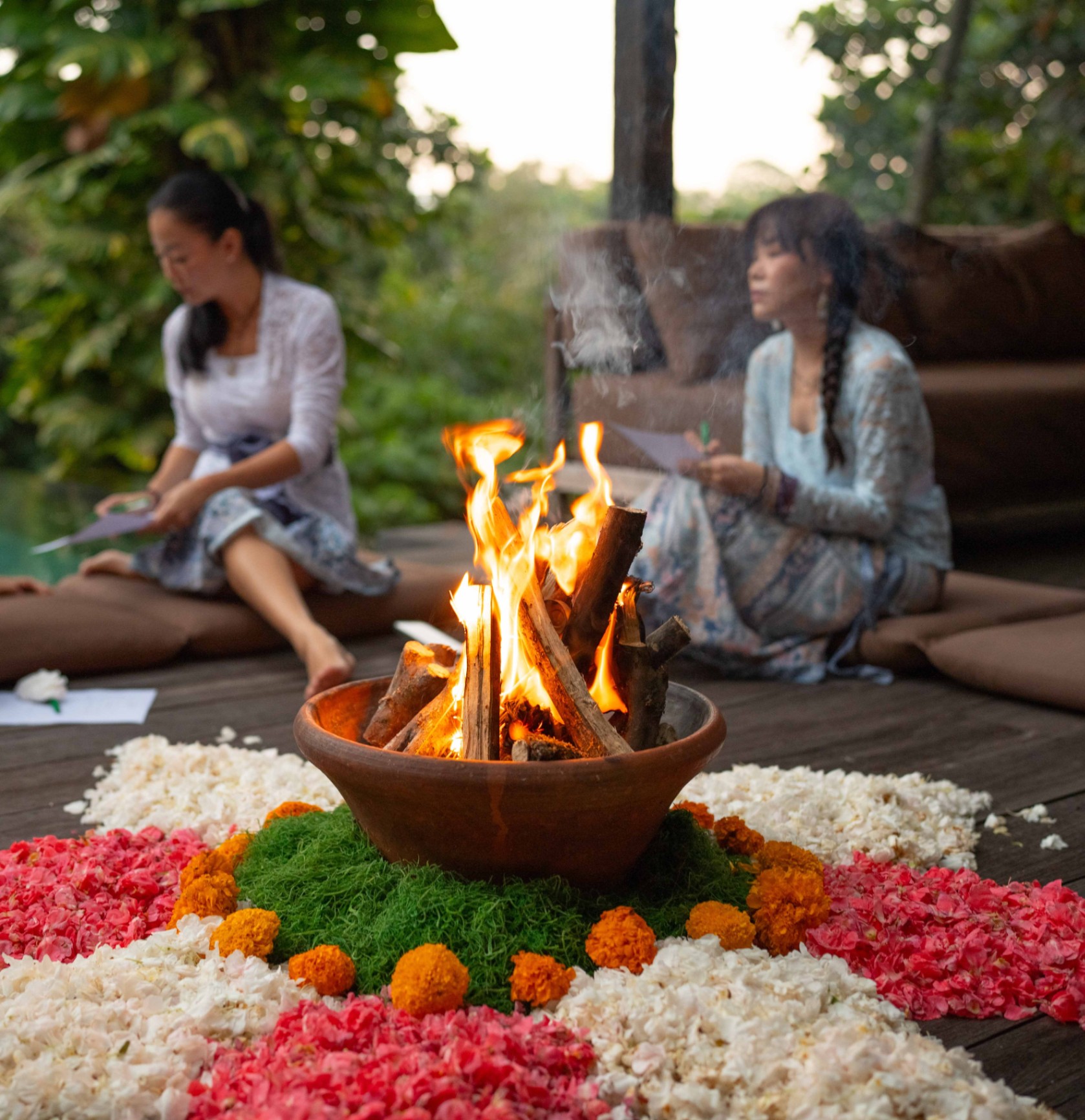 Sacred fire bowl surrounded by flower petals with two women seated in reflection