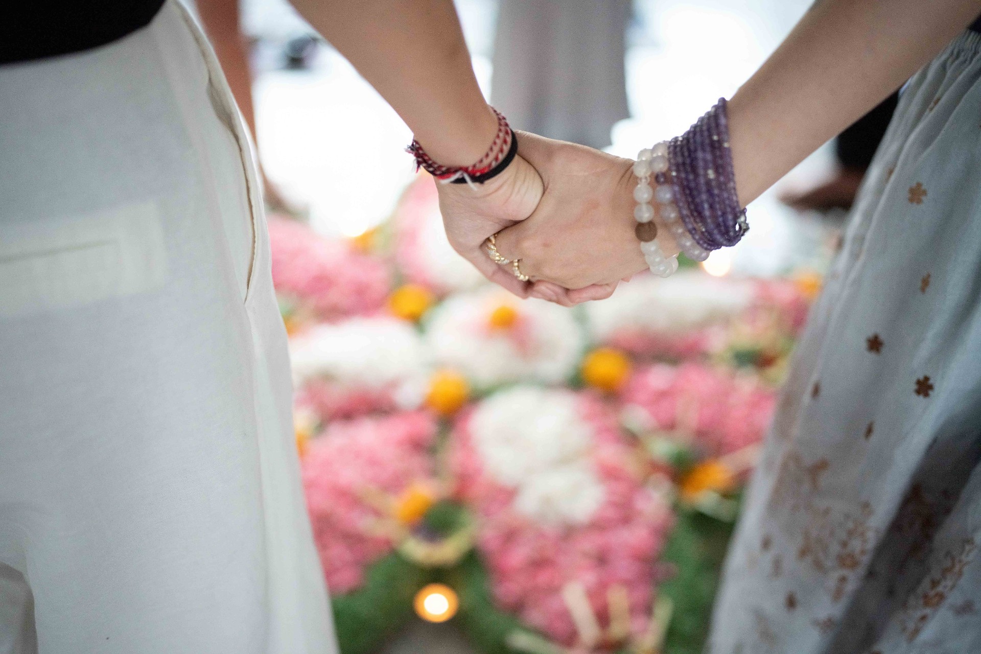 Two women holding hands beside a flower-filled ceremonial offering